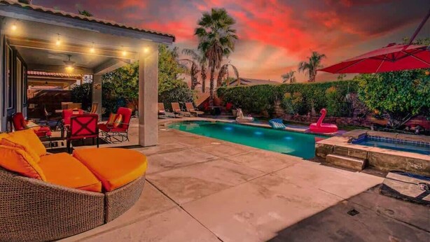 Un espace piscine extérieur doté d’un coin salon abrité, de palmiers et offrant une vue sur un ciel au coucher du soleil.