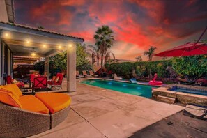 An outdoor pool area with a covered seating area, palm trees, and a sunset sky. - Private Pool, Patio & Game Room | Pet-Friendly (Indio)