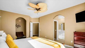 Une chambre d’hôtel avec un grand lit, un ventilateur de plafond, un téléviseur fixé au mur et une vue sur le balcon extérieur.