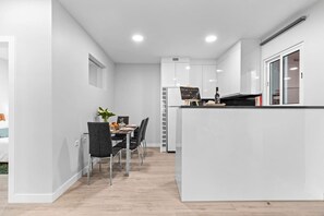 Una cocina moderna con armarios blancos, una isla central y un comedor con sillas y una mesa.