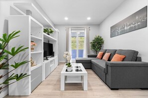Una sala de estar moderna con un sofá gris, una mesa de centro blanca y un televisor sobre un mueble blanco.