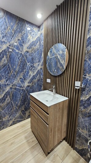 A bathroom with a marble wall, wooden vanity, and a round mirror. - Hacienda corales de margarita (Higüey)
