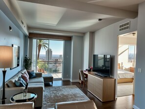 Ein modernes Wohnzimmer mit einer Couch, einem Couchtisch, einem Fernseher und einem Balkon mit Blick auf die Stadt.