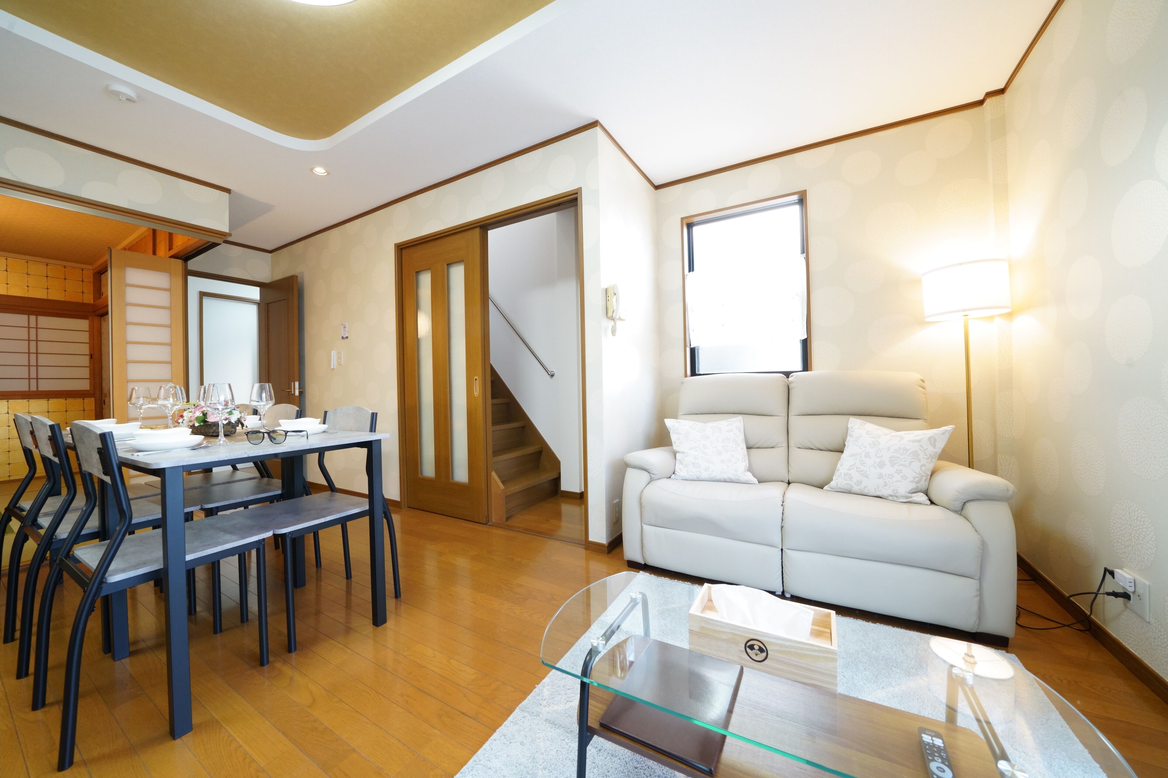 A modern living room with a dining area, a sofa, and a staircase.