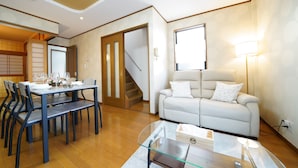 A modern living room with a dining area, a sofa, and a staircase. - KAMON/ 大阪万博まで30分/駐車場有り/大阪城まで徒歩圏内/空港からの送迎サービス有り(有料)/家族向け (Osaka shi Higashinari ku Nakamichi 2)