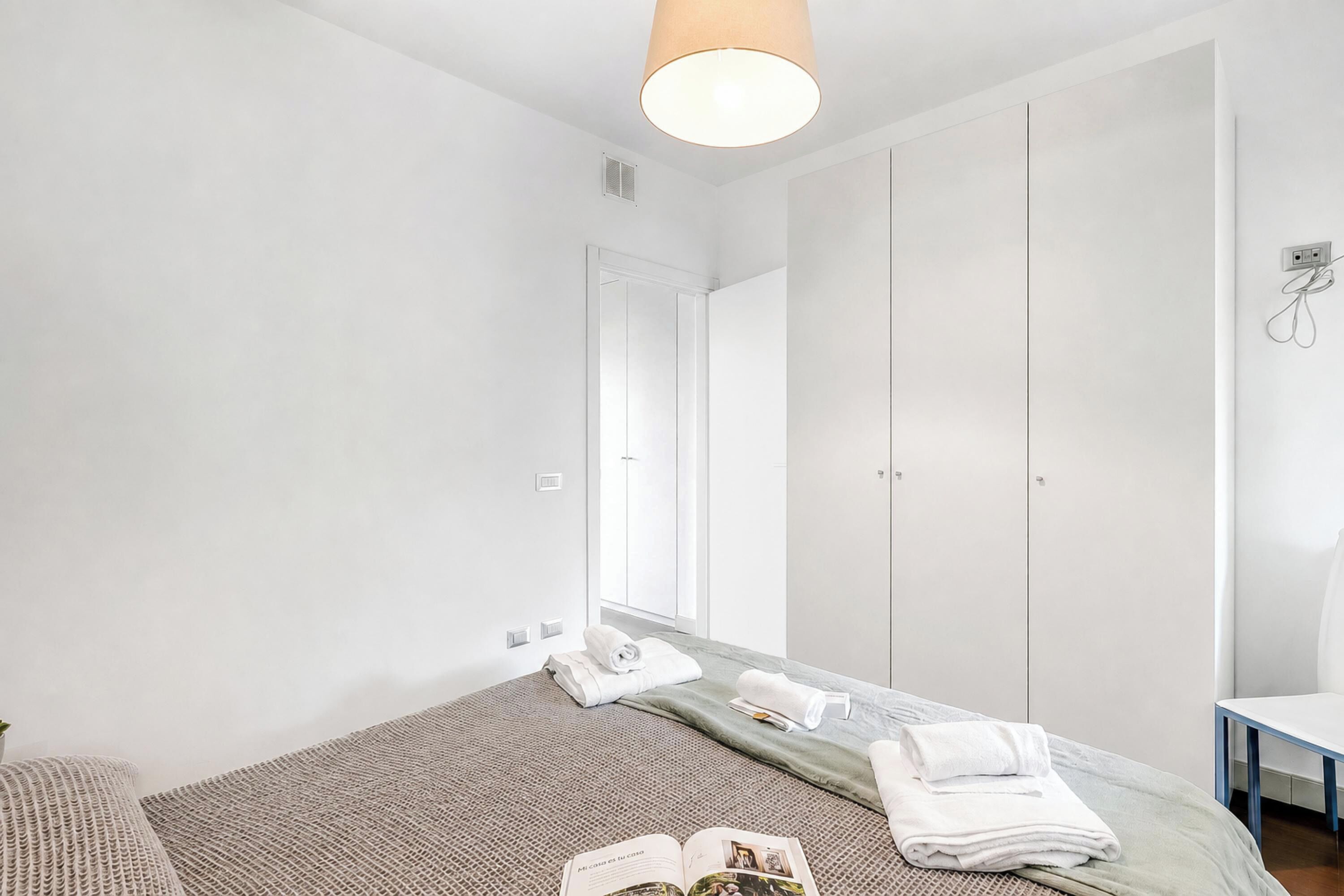 Ein Hotelzimmer mit Bett, Nachttisch, Spiegel, Kleiderschrank und einem Badezimmer inklusive Waschbecken und Handtuchhalter.