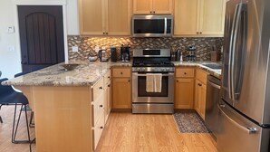 A modern kitchen with wooden cabinets, stainless steel appliances, and a granite countertop. - Fantastic 3 bedroom, 3 bath Coastal Home Close to the Beach and Restaurants (Moss Beach)