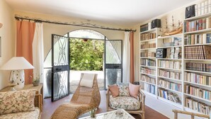 A cozy living room with a wicker sofa, a matching armchair, and a coffee table. A large bookshelf filled with books is visible to the right. - Allumiere by Interhome (Manziana/Canale Monterano)