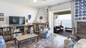 A living room with a television, bookshelves, a coffee table, and a view of the sea through a large window. - The Waves by Interhome (Santa Marinella)