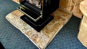 Una estufa de leña con puerta de cristal, sobre un pedestal de piedra, frente a una pared de madera.