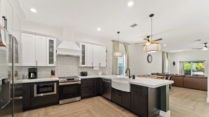 Une cuisine moderne avec des meubles blancs, un îlot central et un coin repas comprenant un canapé et une table.