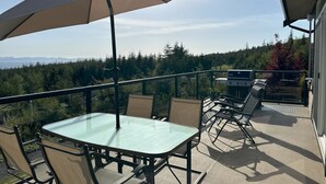 Un patio al aire libre con mesa y sillas, una parrilla y vistas al bosque y las montañas.