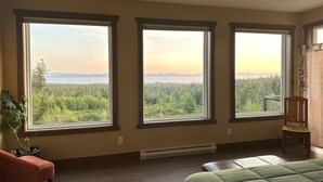 Una habitación con tres ventanas amplias que ofrecen vista a un bosque y una masa de agua distante.