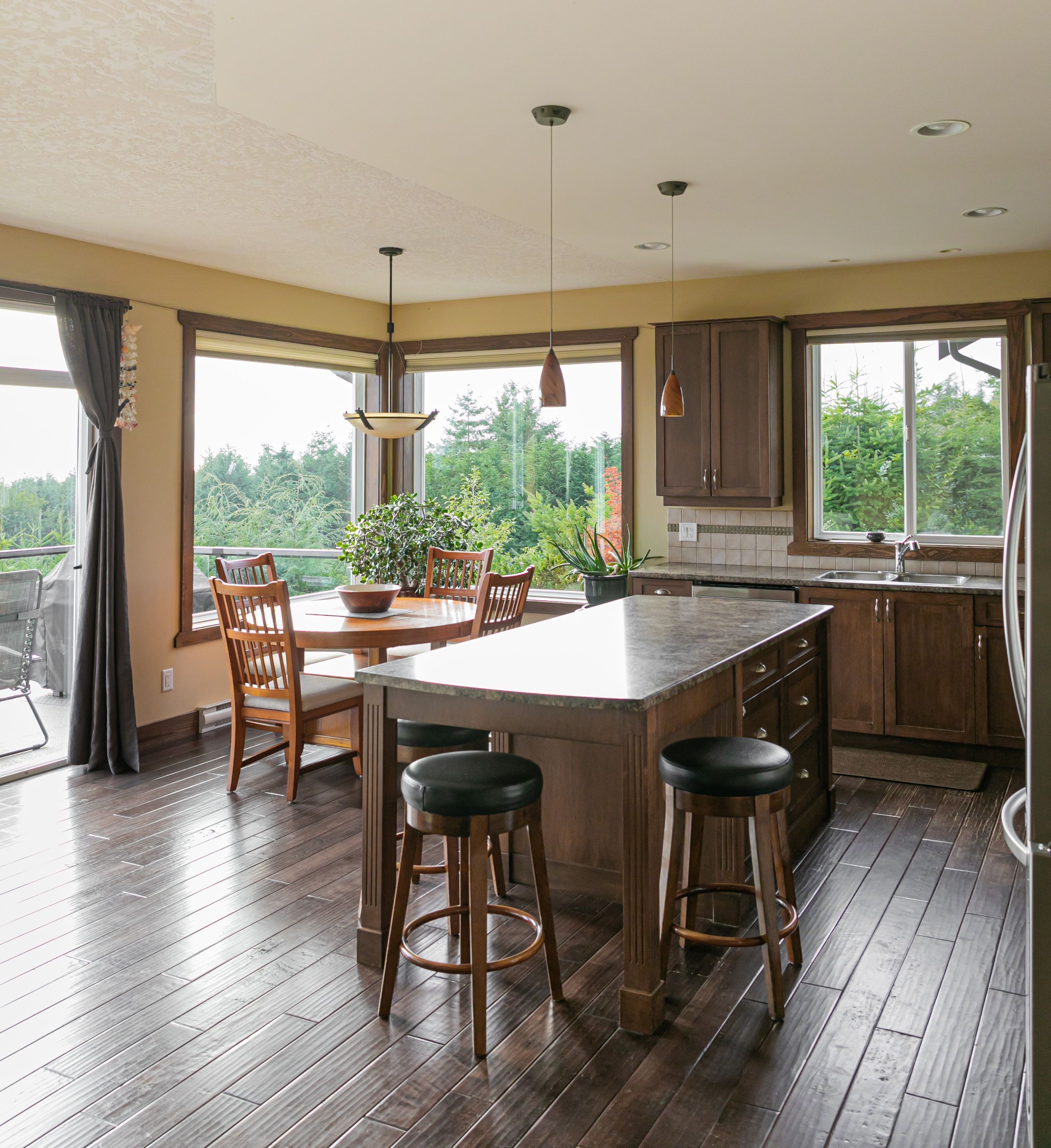 A spacious kitchen with a large island, wooden bar stools, and a view of greenery outside.