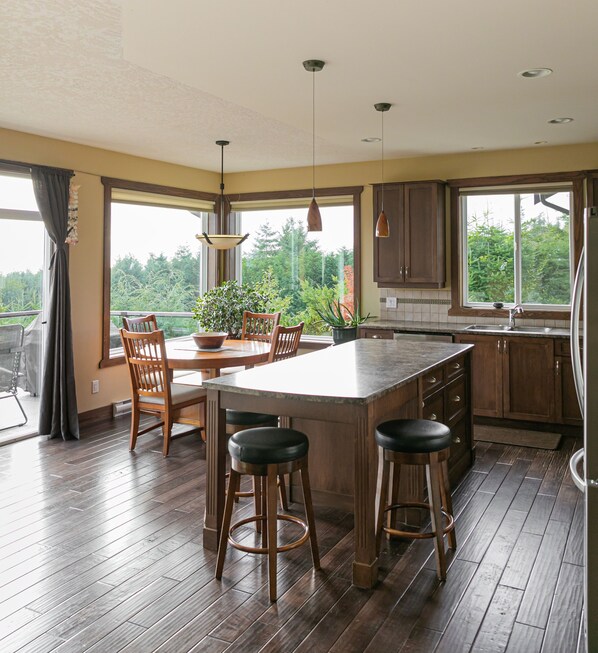A spacious kitchen with a large island, wooden bar stools, and a view of greenery outside.