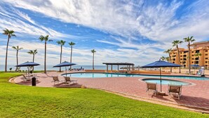 A pool area with lounge chairs and umbrellas, palm trees, and a view of the ocean. - BeachBumCondos (Puerto Penasco)