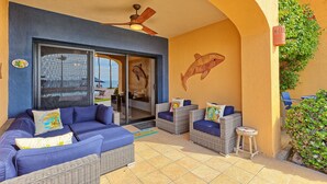 A covered outdoor seating area with wicker furniture and cushions, a ceiling fan, and a dolphin mural on the wall. - BeachBumCondos (Puerto Penasco)