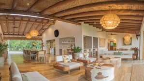 A spacious living area with wooden furniture, a dining table, and a kitchen in the background.