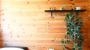 A wooden wall with a shelf holding a clock and a plant. - Do pi-can - Hostel  (Motobu)