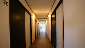 A long, narrow hallway with wooden flooring and dark doors on both sides. - Do pi-can - Hostel  (Motobu)
