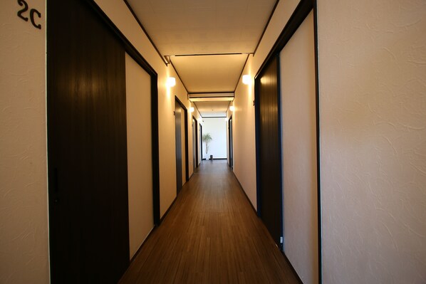 A long, narrow hallway with wooden flooring and dark doors on both sides. - Do pi-can - Hostel  (Motobu)