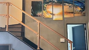A staircase with copper railings and a wall with three framed artworks. - Do pi-can - Hostel  (Motobu)