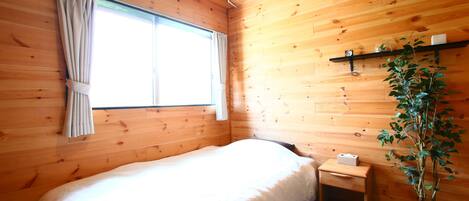 Una habitación con paneles de madera, una cama, una ventana con cortinas, una mesita de noche y una planta en maceta.