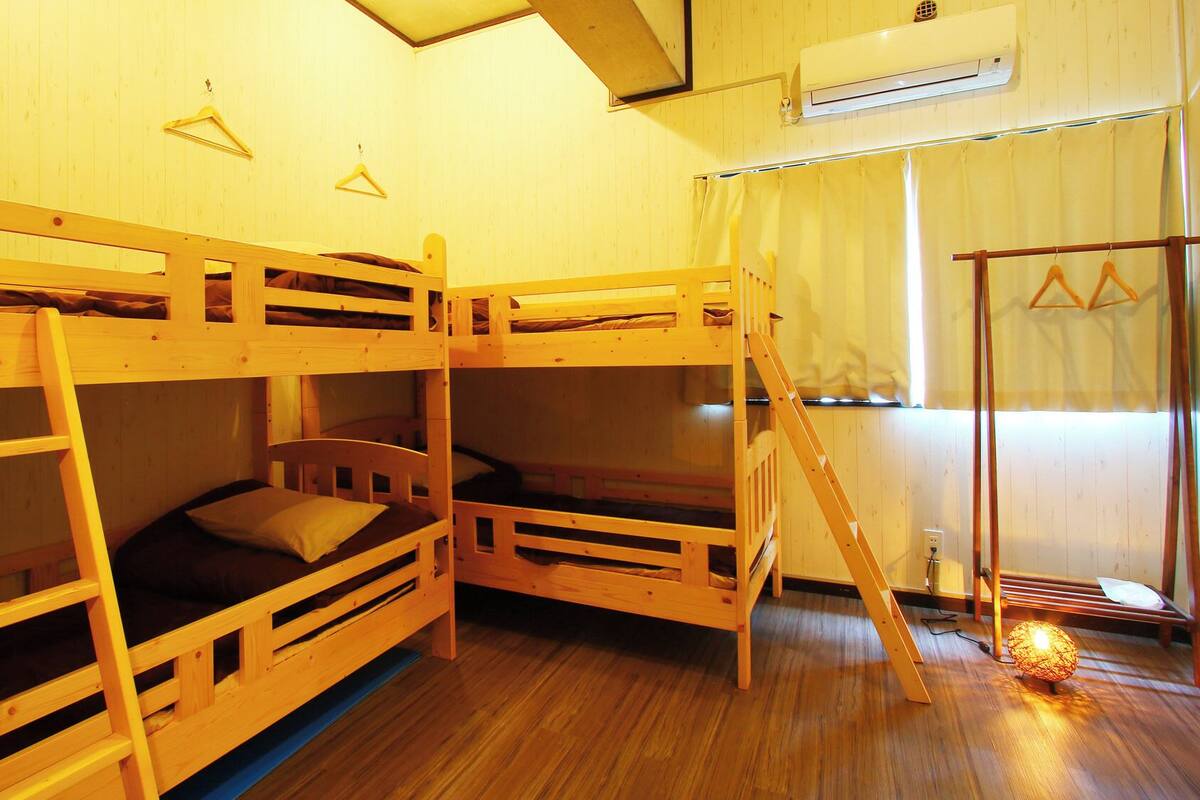A room with bunk beds, a ladder, a window with curtains, and an air conditioning unit.