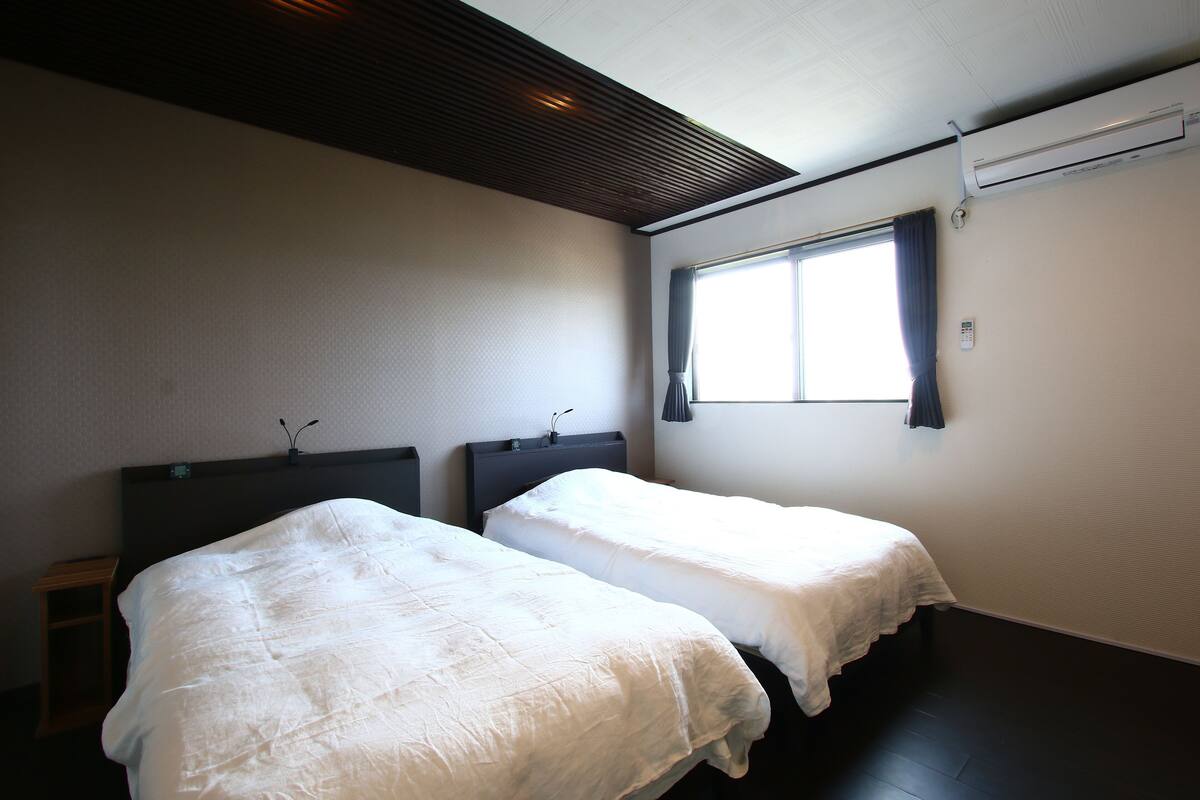 A room with two beds, a window with curtains, and an air conditioning unit.