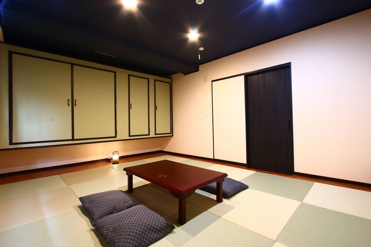 A tatami mat room with a low wooden table and cushions, a sliding door, and traditional sliding doors in the background.