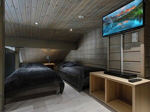 Una habitación con dos camas, un televisor en la pared y techo de madera.
