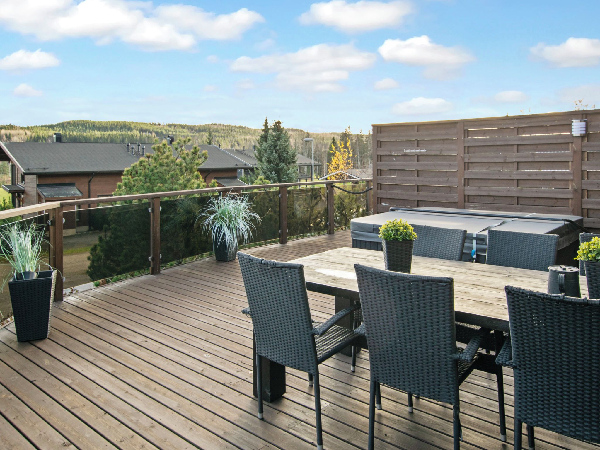 A wooden deck with outdoor furniture, including a table and chairs, and a view of a residential area with houses and trees.