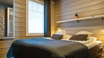 A bedroom with a wooden wall, a window, a bed with a dark bedspread, and a shelf with a plant.