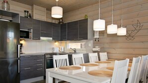 Una cocina moderna con armarios oscuros, electrodomésticos de acero inoxidable y una mesa de comedor blanca con sillas.