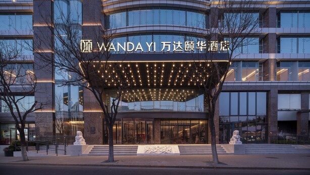 Una entrada de hotel moderna con un corredor cubierto, ventanas de vidrio grandes y un letrero en idioma extranjero.