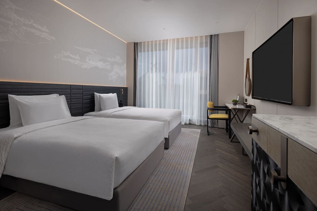 A modern hotel room with two beds, a desk, and a large mirror.
