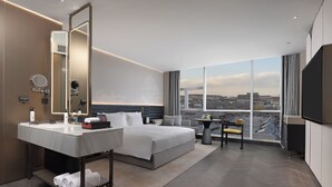 Una habitación de hotel moderna con una cama grande, una tocador con espejo, un televisor de pantalla plana y vistas a la ciudad.