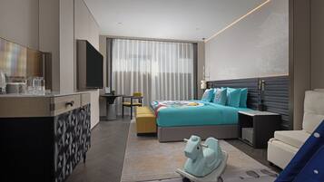Una habitación de hotel moderna con una cama, un escritorio, una silla, un sofá, un televisor y un caballo de juguete decorativo.