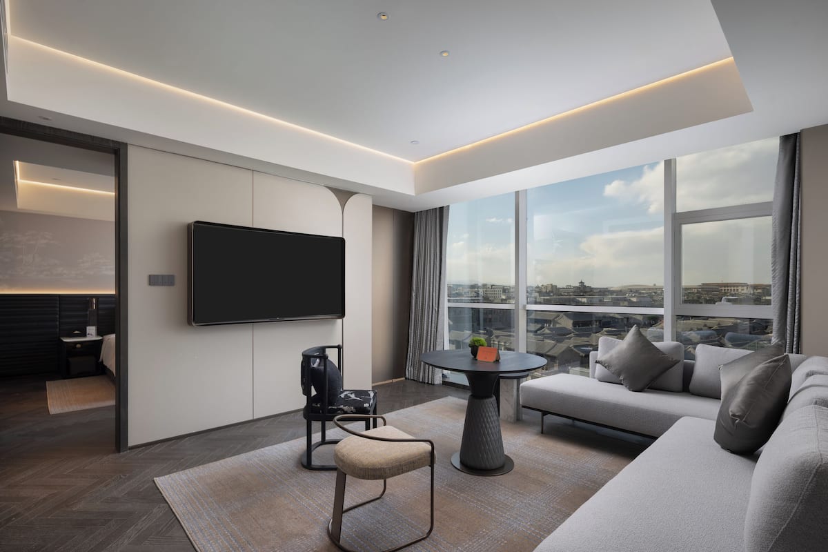 A modern living room with a flat-screen TV, a sofa, a coffee table, and a view of the city through large windows.