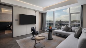 Un salón moderno con un televisor de pantalla plana, un sofá, una mesa de centro y vistas a la ciudad a través de amplios ventanales.