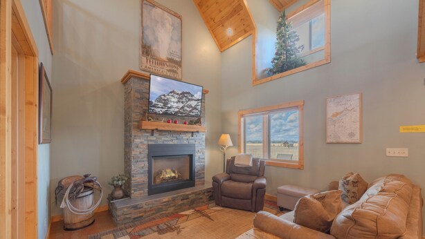 A cozy living room with a stone fireplace, leather sofa, and a mounted TV. - Teton View Ranch! Hot Tub, Mountain Views & 35mi to Yellowstone! (Island Park)