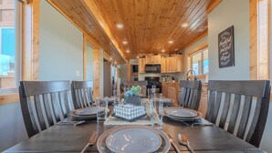 A dining area with a wooden ceiling, a kitchen in the background, and a sign on the wall. - Teton View Ranch! Hot Tub, Mountain Views & 35mi to Yellowstone! (Island Park)