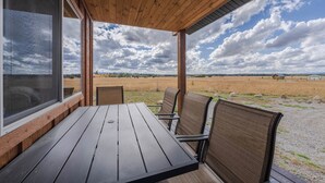 An outdoor covered patio with a table and chairs, overlooking a field. - Teton View Ranch! Hot Tub, Mountain Views & 35mi to Yellowstone! (Island Park)