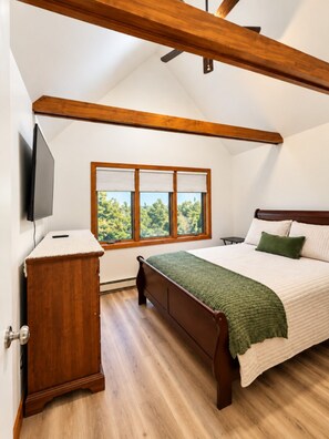 Un dormitorio con cama, cómoda, televisión y ventana con persianas.