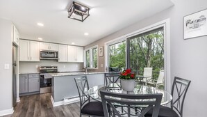 A modern kitchen with white cabinets, stainless steel appliances, and a large island with a glass top table and chairs.