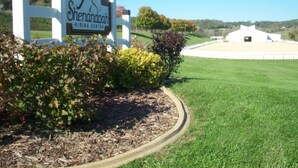A sign for Shenandoah Riding Center with a grassy field and a building in the background.