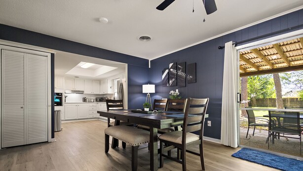 A modern kitchen with white cabinets, a dining area with a dark wooden table and chairs, and a view of the outdoors through a glass door. - NEW - Moody BBQ Retreat w/Covered Patio (Jackson)