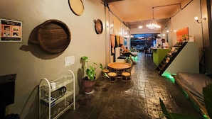 Un intérieur chaleureux avec une barrique en bois, une petite table ronde avec des tabourets, un luminaire suspendu et un escalier menant à un espace bar.