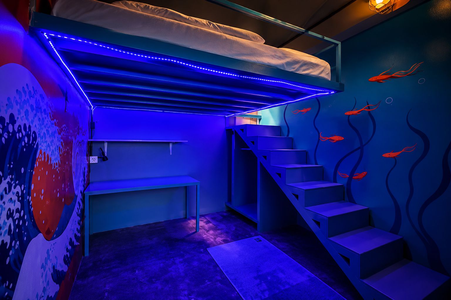 A room with a bunk bed, a staircase, and a wall mural with fish.