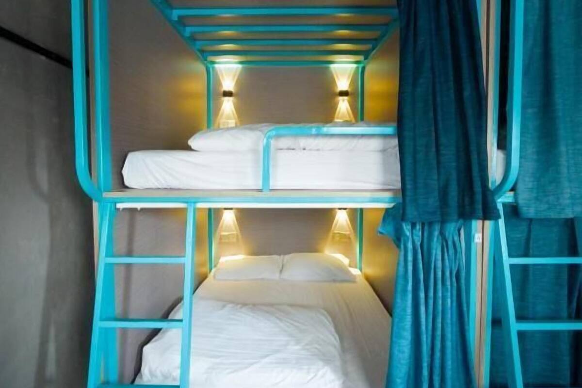 Un letto a castello con una scala, una tenda e due luci fissate al muro.